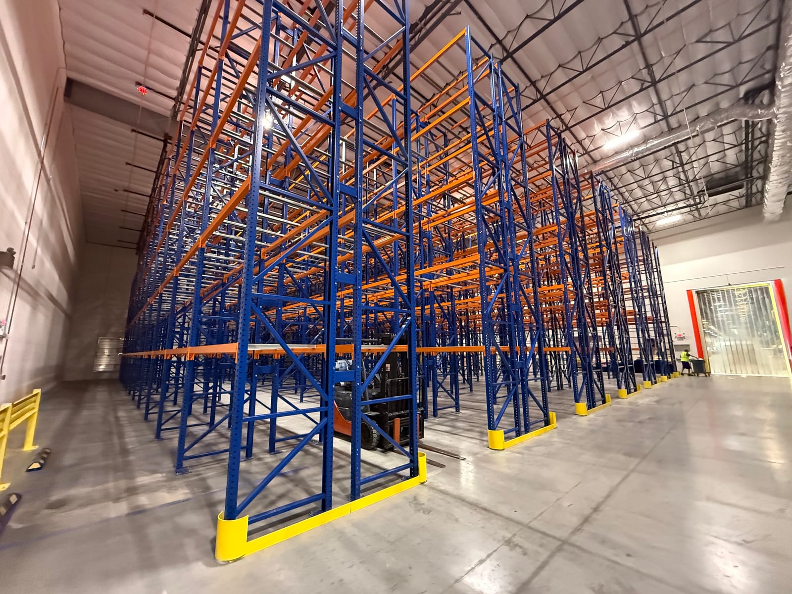 Pallet rack rows running toward a strip-curtain doorway that holds the room's temperature